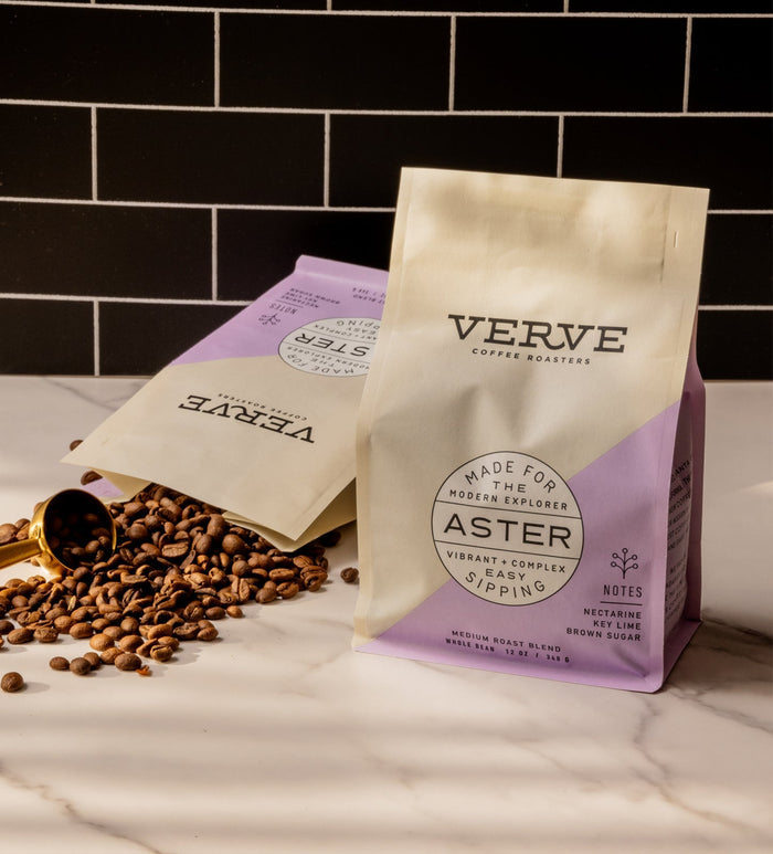 Aster coffee bag by Verve on a white marble counter with a brass scoop and scattered coffee beans.