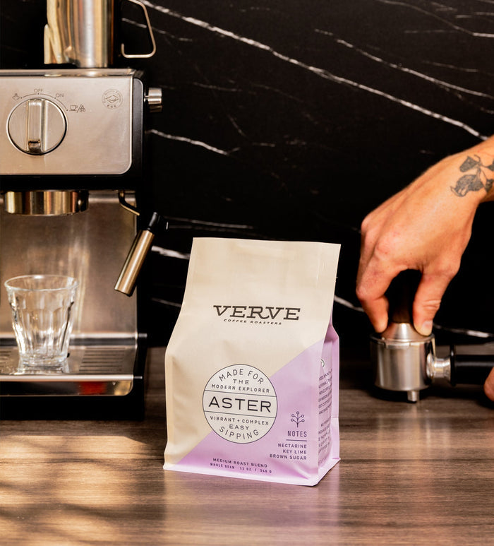 Espresso machine with a Verve Aster coffee bag in the foreground on a dark marble counter.
