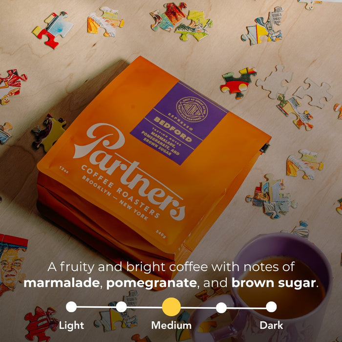 Bedford espresso bag in bright orange with purple label on a puzzle piece background.