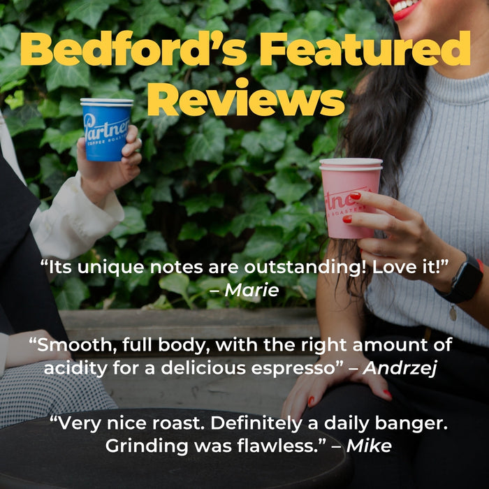 Two people hold colorful espresso cups outdoors as Bedford coffee banner overlays the scene.