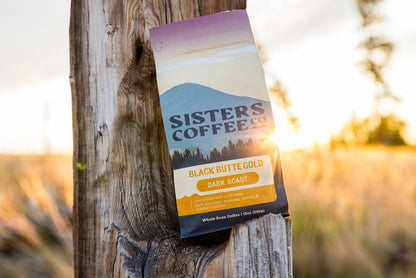 Black Butte Gold coffee bag attached to a weathered wooden post at sunset.