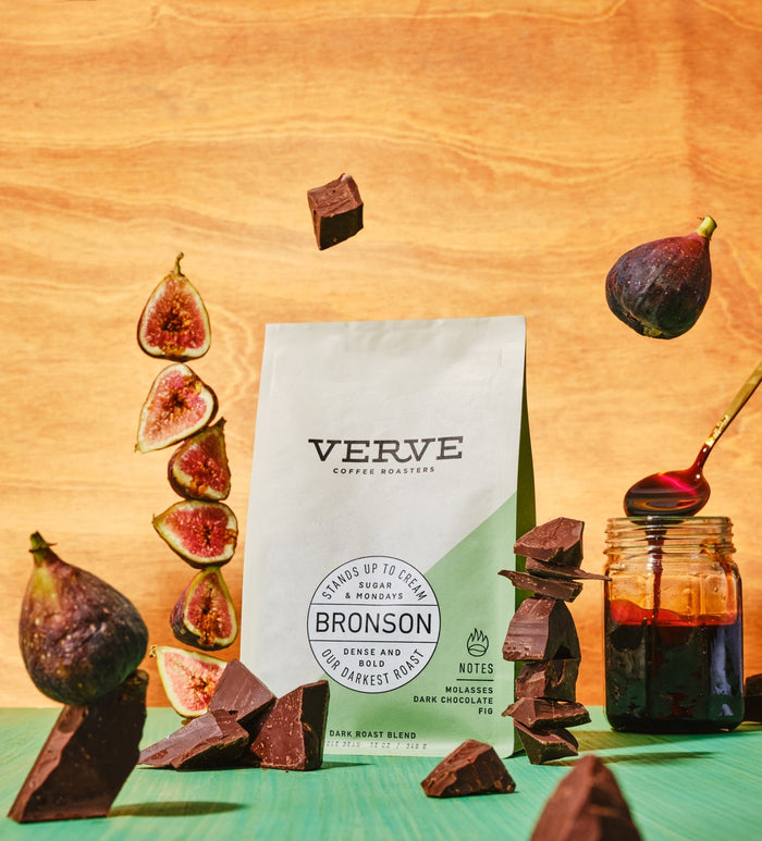 Bronson coffee bag from Verve surrounded by dark chocolate pieces and fig slices on a warm wooden surface
