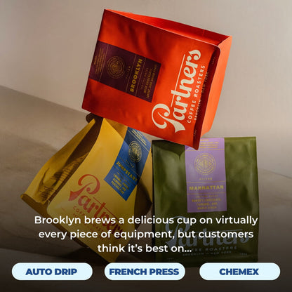 Red Brooklyn coffee bag resting atop yellow and green coffee bags.