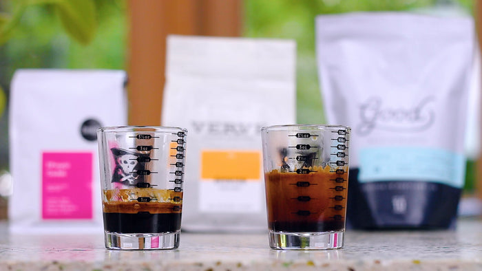 Two espresso glasses with crema on a counter with blurred packaging in the background
