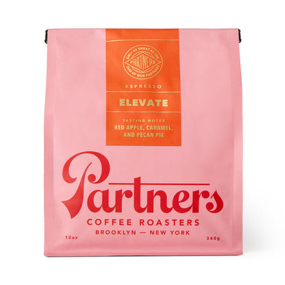 Pink Elevate coffee bag from Partners Coffee Roasters with an orange tasting notes panel listing red apple caramel and pecan pie.