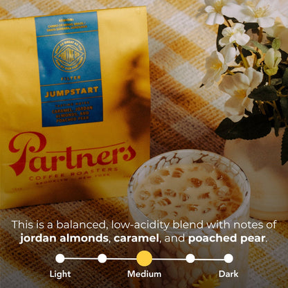 Jumpstart yellow coffee bag with blue label next to a blue crate and a hand holding a red Partners bag