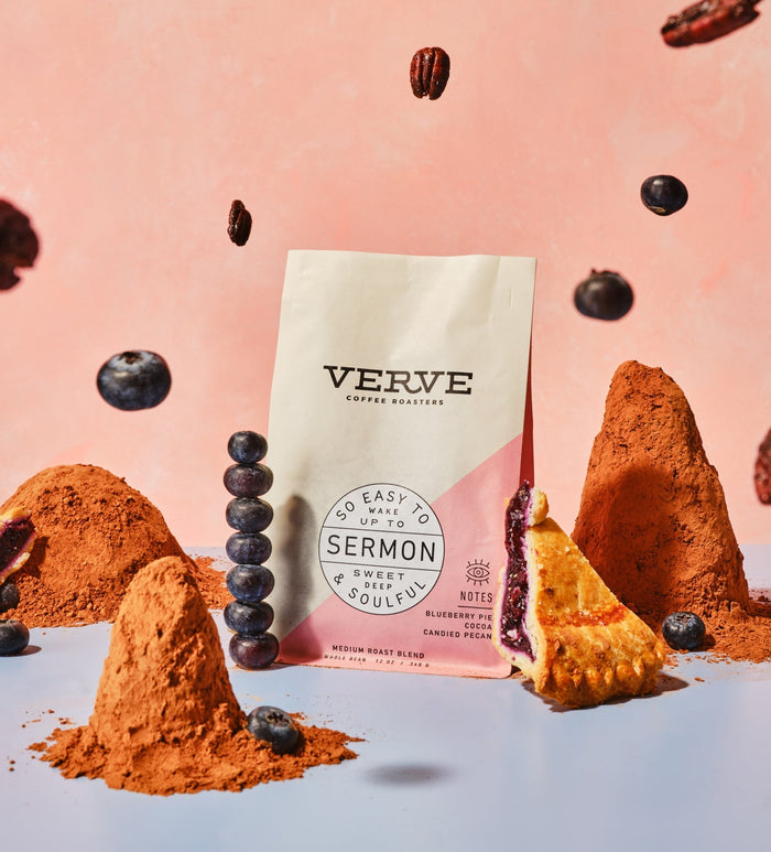 Sermon Espresso bag with pink diagonal panel surrounded by cocoa powder and pastries against a pink background.